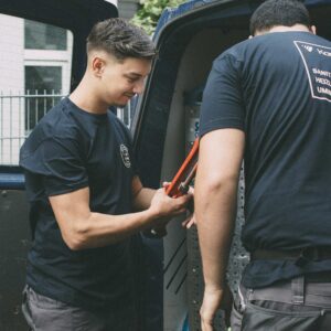 Zwei Männer in dunklen T-Shirts arbeiten konzentriert an einem Van.