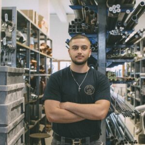 Ein jüngerer Mann mit ernstem Blick steht in einem Industrie-Umfeld.